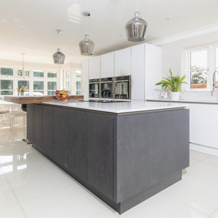 Large modern galley eat-in kitchen in Hampshire with an integrated sink, flat-panel cabinets, white cabinets, granite benchtops, white splashback, granite splashback, stainless steel appliances, ceramic floors, with island, beige floor and white benchtop.