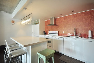 Example of a small trendy single-wall dark wood floor open concept kitchen design in Vancouver with an undermount sink, flat-panel cabinets, white cabinets, granite countertops, orange backsplash, ceramic backsplash, white appliances and an island