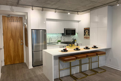 Example of a small trendy galley vinyl floor and gray floor open concept kitchen design in Toronto with an undermount sink, flat-panel cabinets, white cabinets, quartz countertops, gray backsplash, ceramic backsplash, stainless steel appliances, an island and white countertops