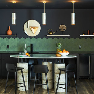 Photo of a small contemporary single-wall open plan kitchen in New York with an undermount sink, louvered cabinets, black cabinets, soapstone benchtops, green splashback, ceramic splashback, stainless steel appliances, medium hardwood floors, with island, brown floor and black benchtop.