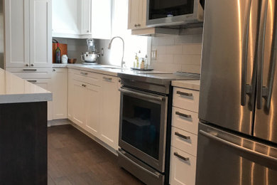 Example of a trendy l-shaped medium tone wood floor and brown floor open concept kitchen design in Toronto with an undermount sink, shaker cabinets, white cabinets, quartz countertops, white backsplash, subway tile backsplash, stainless steel appliances, an island and white countertops