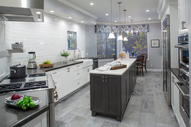 Mid-sized transitional galley porcelain tile enclosed kitchen photo in Los Angeles with a farmhouse sink, shaker cabinets, gray cabinets, quartz countertops, white backsplash, ceramic backsplash, stainless steel appliances and an island