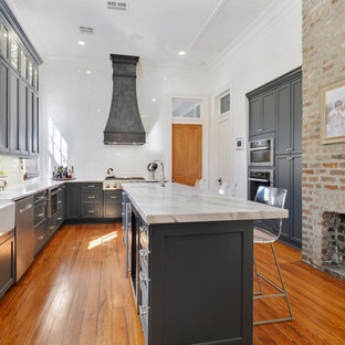 Imagen de cocina en U, campestre, grande, con fregadero sobremueble, puertas de armario azules, salpicadero blanco, electrodomésticos de acero inoxidable, una isla, armarios estilo shaker, suelo de madera en tonos medios y suelo marrón