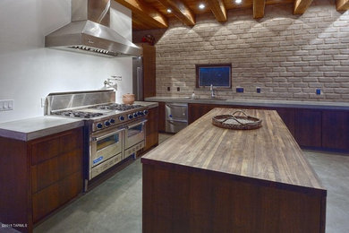 Immagine di una grande cucina design con lavello da incasso, ante lisce, ante in legno scuro, top in cemento, elettrodomestici in acciaio inossidabile e pavimento in cemento