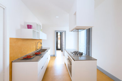 Photo of a medium sized contemporary galley enclosed kitchen in Other with flat-panel cabinets, white cabinets, yellow splashback, stainless steel appliances, concrete flooring, an island, yellow floors and a submerged sink.