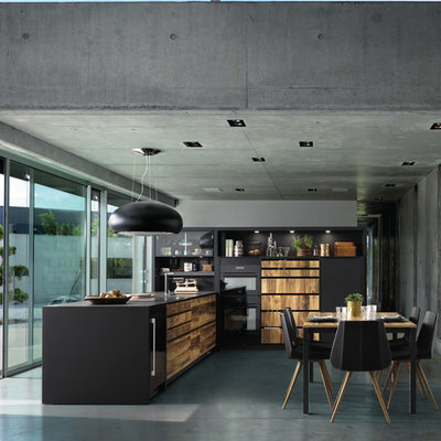 Example of a mid-sized trendy l-shaped concrete floor and gray floor open concept kitchen design in London with black cabinets, quartz countertops, black appliances, an undermount sink, flat-panel cabinets, gray backsplash and a peninsula