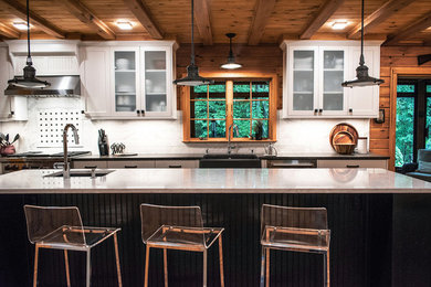 Mountain style medium tone wood floor and brown floor eat-in kitchen photo in New York with a farmhouse sink, recessed-panel cabinets, white cabinets, quartz countertops, white backsplash, marble backsplash, stainless steel appliances, an island and white countertops
