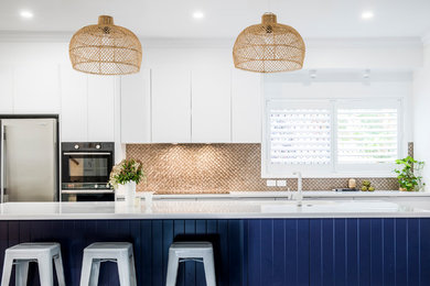 Photo of a medium sized contemporary galley open plan kitchen in Townsville with a submerged sink, flat-panel cabinets, blue cabinets, engineered stone countertops, metallic splashback, mosaic tiled splashback, stainless steel appliances, an island and white worktops.