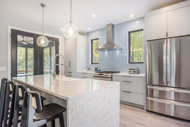 Immagine di un cucina con isola centrale minimalista con ante grigie, top in quarzo composito, paraspruzzi blu, elettrodomestici in acciaio inossidabile, pavimento in vinile, pavimento marrone e top bianco