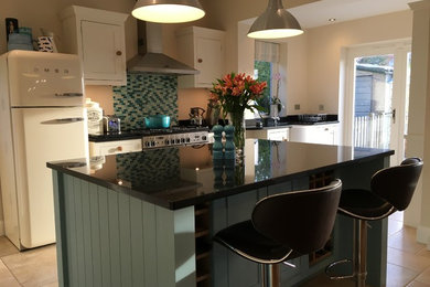 Photo of a farmhouse open plan kitchen in Kent with a belfast sink, shaker cabinets, granite worktops, blue splashback, glass tiled splashback, ceramic flooring and an island.