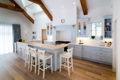 Photo of a farmhouse galley kitchen in Cork with shaker cabinets, grey cabinets, white splashback, metro tiled splashback, stainless steel appliances, medium hardwood flooring, an island, brown floors and white worktops.