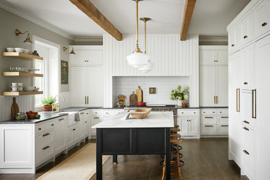 Idée de décoration pour une grande cuisine encastrable tradition en U avec un évier de ferme, un placard à porte shaker, des portes de placard blanches, un plan de travail en quartz, une crédence blanche, une crédence en carrelage métro, un sol en bois brun, îlot et plan de travail noir.