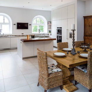 This is an example of a medium sized contemporary u-shaped kitchen/diner in Devon with flat-panel cabinets, white cabinets, granite worktops, porcelain flooring, an island, integrated appliances and beige floors.