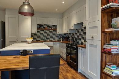 Medium sized contemporary l-shaped open plan kitchen in Other with a belfast sink, shaker cabinets, grey cabinets, wood worktops, multi-coloured splashback, ceramic splashback, integrated appliances, laminate floors, an island, multi-coloured floors and multicoloured worktops.