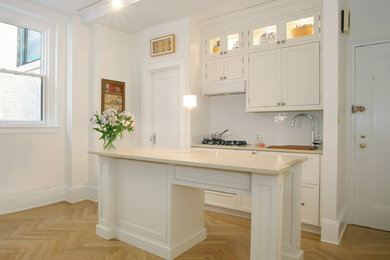 Small transitional single-wall light wood floor and brown floor kitchen photo in New York with shaker cabinets, white cabinets, white backsplash and an island