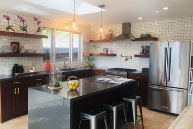 Mid-sized trendy l-shaped porcelain tile and beige floor open concept kitchen photo with an undermount sink, shaker cabinets, dark wood cabinets, white backsplash, subway tile backsplash, stainless steel appliances, an island and black countertops