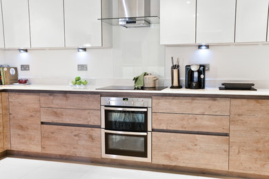 Foto på ett mellanstort funkis l-kök, med släta luckor, skåp i ljust trä, bänkskiva i koppar, vitt stänkskydd, glaspanel som stänkskydd och rostfria vitvaror