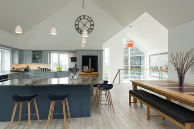 Design ideas for a large contemporary l-shaped kitchen/diner in West Midlands with recessed-panel cabinets, blue cabinets, black appliances, light hardwood flooring, an island, a submerged sink and marble worktops.