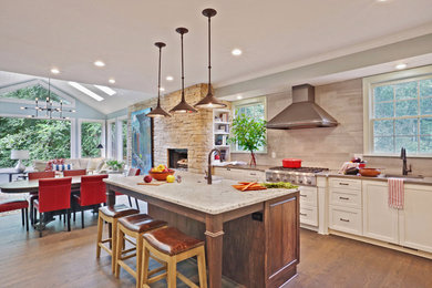 Inspiration for a large transitional l-shaped medium tone wood floor open concept kitchen remodel in Atlanta with a farmhouse sink, shaker cabinets, white cabinets, quartz countertops, gray backsplash, stainless steel appliances, an island and limestone backsplash