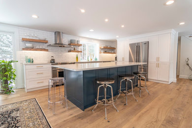 Open concept kitchen - mid-sized farmhouse single-wall light wood floor and brown floor open concept kitchen idea in Boston with shaker cabinets, white cabinets, white backsplash, subway tile backsplash, stainless steel appliances, an island and gray countertops