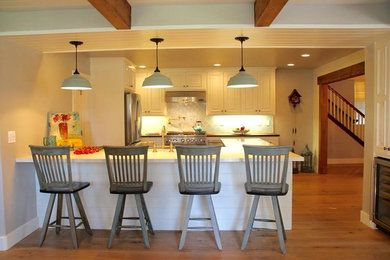 Eat-in kitchen - country light wood floor eat-in kitchen idea in San Luis Obispo with a farmhouse sink, raised-panel cabinets, white cabinets, quartz countertops, blue backsplash, glass tile backsplash, stainless steel appliances and a peninsula