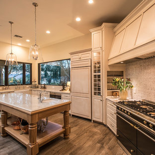 Photo of a large country u-shaped open plan kitchen in Phoenix with a farmhouse sink, raised-panel cabinets, beige cabinets, marble benchtops, panelled appliances, travertine floors, with island, brown floor and white benchtop.