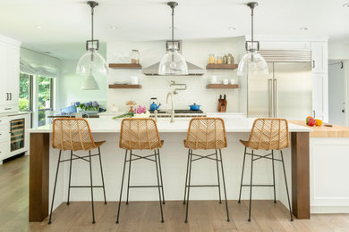 Inspiration for a large transitional u-shaped medium tone wood floor and brown floor eat-in kitchen remodel in New York with a farmhouse sink, shaker cabinets, white cabinets, quartzite countertops, white backsplash, ceramic backsplash, stainless steel appliances, an island and white countertops