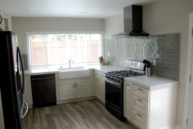 This is an example of a medium sized classic grey and cream u-shaped enclosed kitchen in San Francisco with a belfast sink, recessed-panel cabinets, yellow cabinets, engineered stone countertops, green splashback, glass tiled splashback, stainless steel appliances, porcelain flooring, no island and multi-coloured floors.