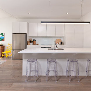 Inspiration for a mid-sized scandinavian single-wall eat-in kitchen in Other with a double-bowl sink, flat-panel cabinets, white cabinets, quartz benchtops, white splashback, glass sheet splashback, stainless steel appliances, laminate floors, with island, grey floor and white benchtop.