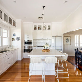 Traditional l-shaped kitchen in Brisbane with an undermount sink, shaker cabinets, white cabinets, white splashback, stainless steel appliances, medium hardwood floors, with island, brown floor and white benchtop.