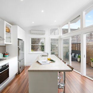 Photo of a contemporary galley kitchen in Sydney with a double-bowl sink, flat-panel cabinets, white cabinets, marble benchtops, brown splashback, stainless steel appliances, medium hardwood floors, with island, brown floor and beige benchtop.