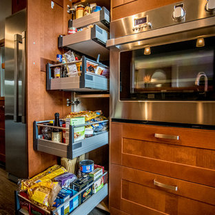 Cette image montre une grand cuisine américaine parallèle design avec un évier 2 bacs, un placard à porte shaker, un plan de travail en quartz modifié, un électroménager en acier inoxydable, des portes de placard marrons, une crédence verte, une crédence en carreau de verre, sol en stratifié, aucun îlot, un sol marron et un plan de travail blanc.