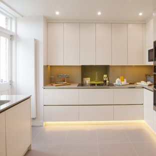 Classic u-shaped kitchen in London with a submerged sink, flat-panel cabinets, white cabinets, beige splashback, stainless steel appliances, beige floors and beige worktops.