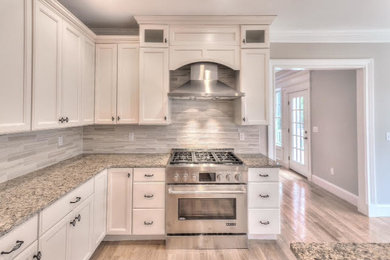 Enclosed kitchen - large traditional u-shaped light wood floor enclosed kitchen idea in Boston with recessed-panel cabinets, white cabinets, granite countertops, gray backsplash, ceramic backsplash, stainless steel appliances and an island