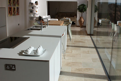 Inredning av ett modernt mellanstort kök, med en nedsänkt diskho, släta luckor, vita skåp, marmorbänkskiva, rostfria vitvaror, travertin golv och en köksö