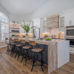 Photo of a large transitional l-shaped kitchen with an integrated sink, shaker cabinets, white cabinets, quartzite benchtops, white splashback, porcelain splashback, stainless steel appliances, vinyl floors, with island, brown floor and white benchtop.