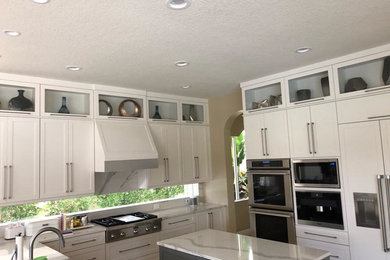 This is an example of a medium sized contemporary l-shaped enclosed kitchen in Miami with a belfast sink, shaker cabinets, white cabinets, marble worktops, window splashback, stainless steel appliances, an island and white worktops.
