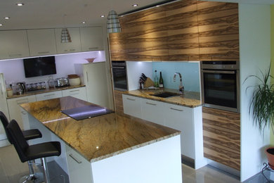 Foto på ett mellanstort funkis kök, med en integrerad diskho, släta luckor, skåp i ljust trä, granitbänkskiva, glaspanel som stänkskydd, rostfria vitvaror, klinkergolv i porslin och en köksö