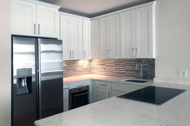 Example of a small trendy u-shaped light wood floor and brown floor kitchen design in New York with a drop-in sink, shaker cabinets, white cabinets, quartz countertops, metallic backsplash, stainless steel appliances and a peninsula