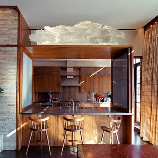 This is an example of a contemporary galley kitchen in New York with an integrated sink, flat-panel cabinets, medium wood cabinets, stainless steel benchtops, metallic splashback and stainless steel appliances.