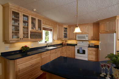 Example of a mid-sized classic l-shaped dark wood floor and brown floor enclosed kitchen design in San Diego with a double-bowl sink, raised-panel cabinets, light wood cabinets, limestone countertops, white appliances, an island and black countertops