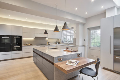 Photo of a contemporary l-shaped kitchen in London with a submerged sink, flat-panel cabinets, white cabinets, grey splashback, stainless steel appliances, light hardwood flooring, an island and beige floors.