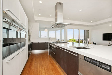 Example of a large trendy galley light wood floor open concept kitchen design in San Francisco with an integrated sink, flat-panel cabinets, dark wood cabinets, quartz countertops, white backsplash, stainless steel appliances and an island