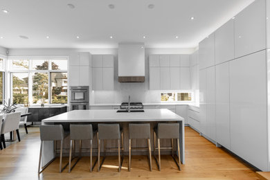 Example of a large trendy l-shaped light wood floor and beige floor eat-in kitchen design in Toronto with an undermount sink, flat-panel cabinets, white cabinets, quartz countertops, white backsplash, quartz backsplash, paneled appliances, an island and white countertops
