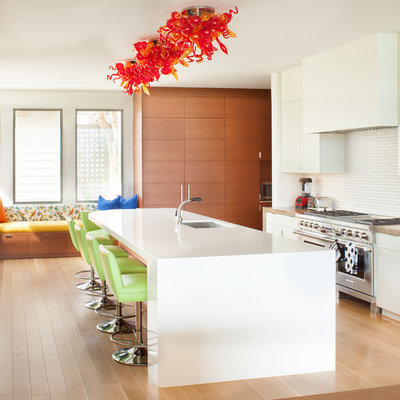 Open concept kitchen - mid-sized contemporary u-shaped light wood floor open concept kitchen idea in Los Angeles with an undermount sink, flat-panel cabinets, white cabinets, white backsplash, stainless steel appliances, an island, solid surface countertops and ceramic backsplash