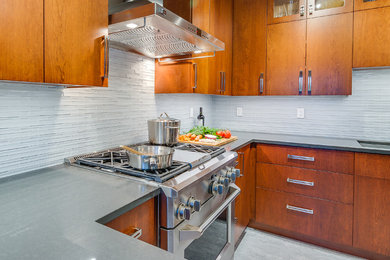 Example of a mid-sized trendy l-shaped slate floor eat-in kitchen design in Seattle with an undermount sink, flat-panel cabinets, medium tone wood cabinets, solid surface countertops, gray backsplash, glass tile backsplash, stainless steel appliances and two islands