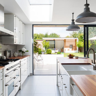 Design ideas for a medium sized contemporary galley open plan kitchen in London with a belfast sink, flat-panel cabinets, white cabinets, wood worktops, grey splashback, metro tiled splashback and an island.