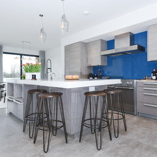 Contemporary kitchen in Berkshire with flat-panel cabinets, grey cabinets, blue splashback, glass sheet splashback, integrated appliances, an island, grey floors and white worktops.