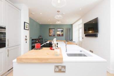 Photo of a medium sized traditional single-wall kitchen/diner in Edinburgh with a built-in sink, recessed-panel cabinets, white cabinets, engineered stone countertops, integrated appliances and an island.