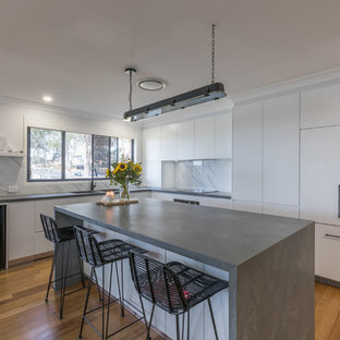This is an example of a contemporary l-shaped kitchen in Sydney with an undermount sink, flat-panel cabinets, white cabinets, white splashback, stainless steel appliances, medium hardwood floors, with island, brown floor and grey benchtop.